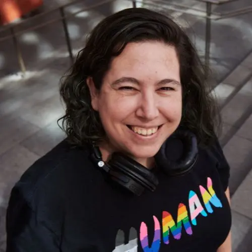 Marta Torre sonriendo son unos auriculares en el cuello y una camiseta negra con la palabra human y la bandera lgtbiq+