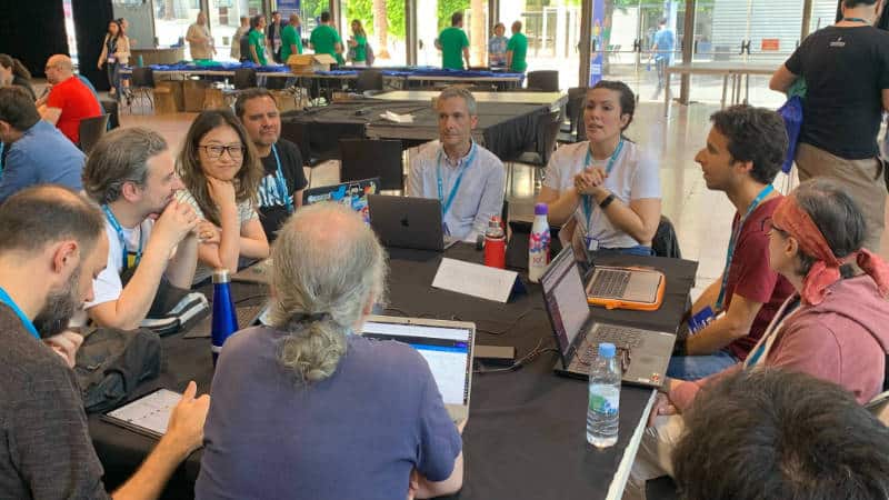 Mesa de sostenibilidad en la WordCamp Barcelona 2023. Hay un grupo de personas alrededor de unas mesas.